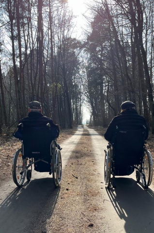 Zwei Senioren im Rollstuhl bei einem Spaziergang im Wald